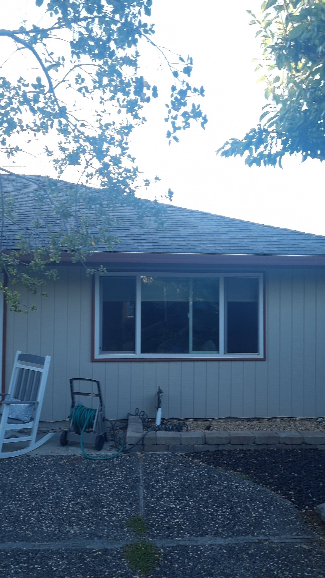 Photo of a house wall with a window and a rocking chair, over a gravel patio.